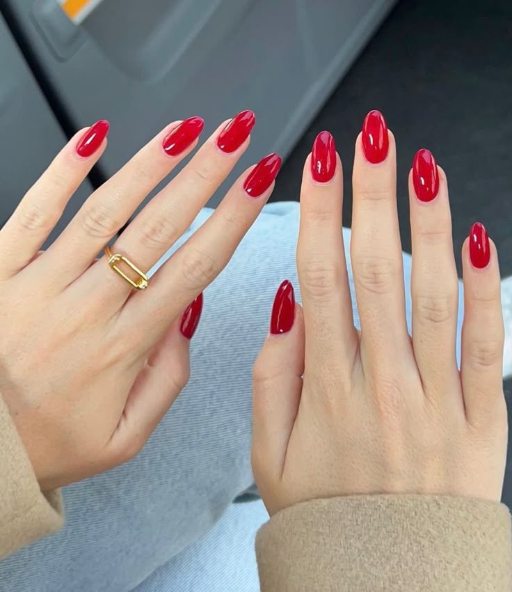 Elegante rote Nägel in Mandelform mit glänzendem Finish und Goldschmuck.